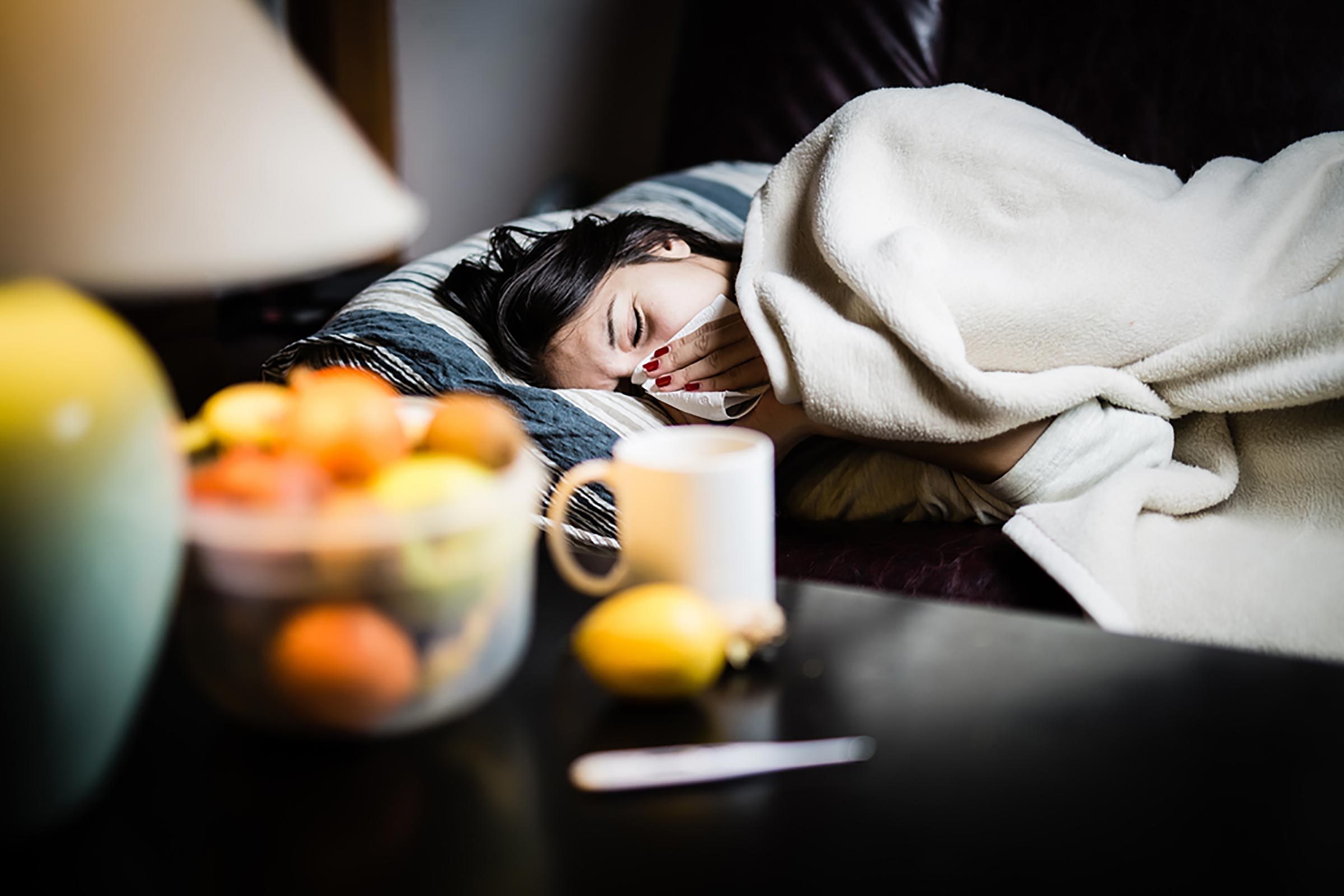 woman covered up in bed, sneezing into a handkerchief 
