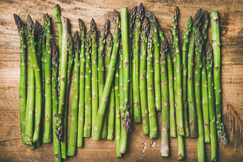 Seasonal harvest produce . Flat-lay of raw uncooked green asparagus in row over rustic wooden background, top view. Local market food concept