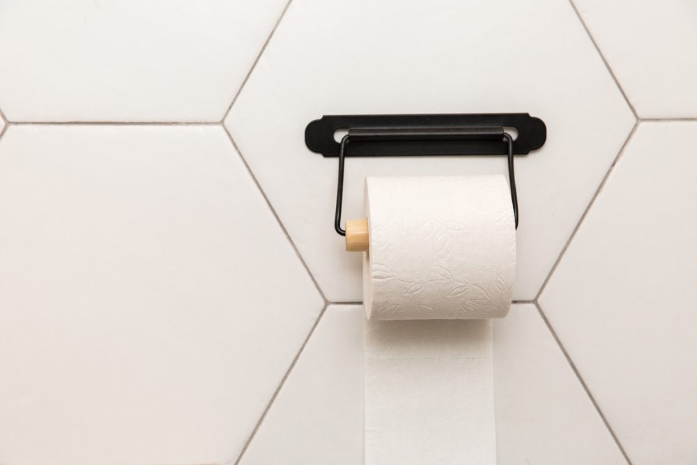 A white roll of soft toilet paper neatly hanging on a modern chrome holder on a light bathroom wall.