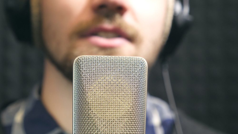 Young man emotionally recording new song. Working of creative musician. Male singer in headphones singing song into the microphone at sound studio. Show business concept. Slow motion Close up.