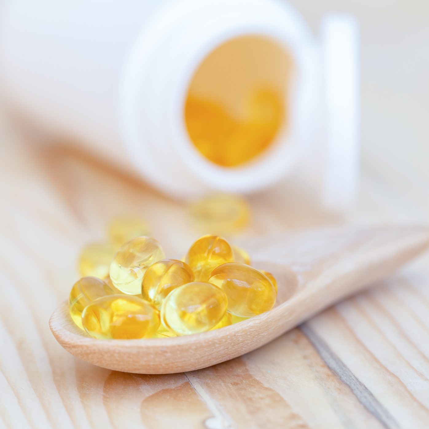 Fish oil capsules with omega 3 and vitamin D on spoon wood with wooden background, healthy diet concept.