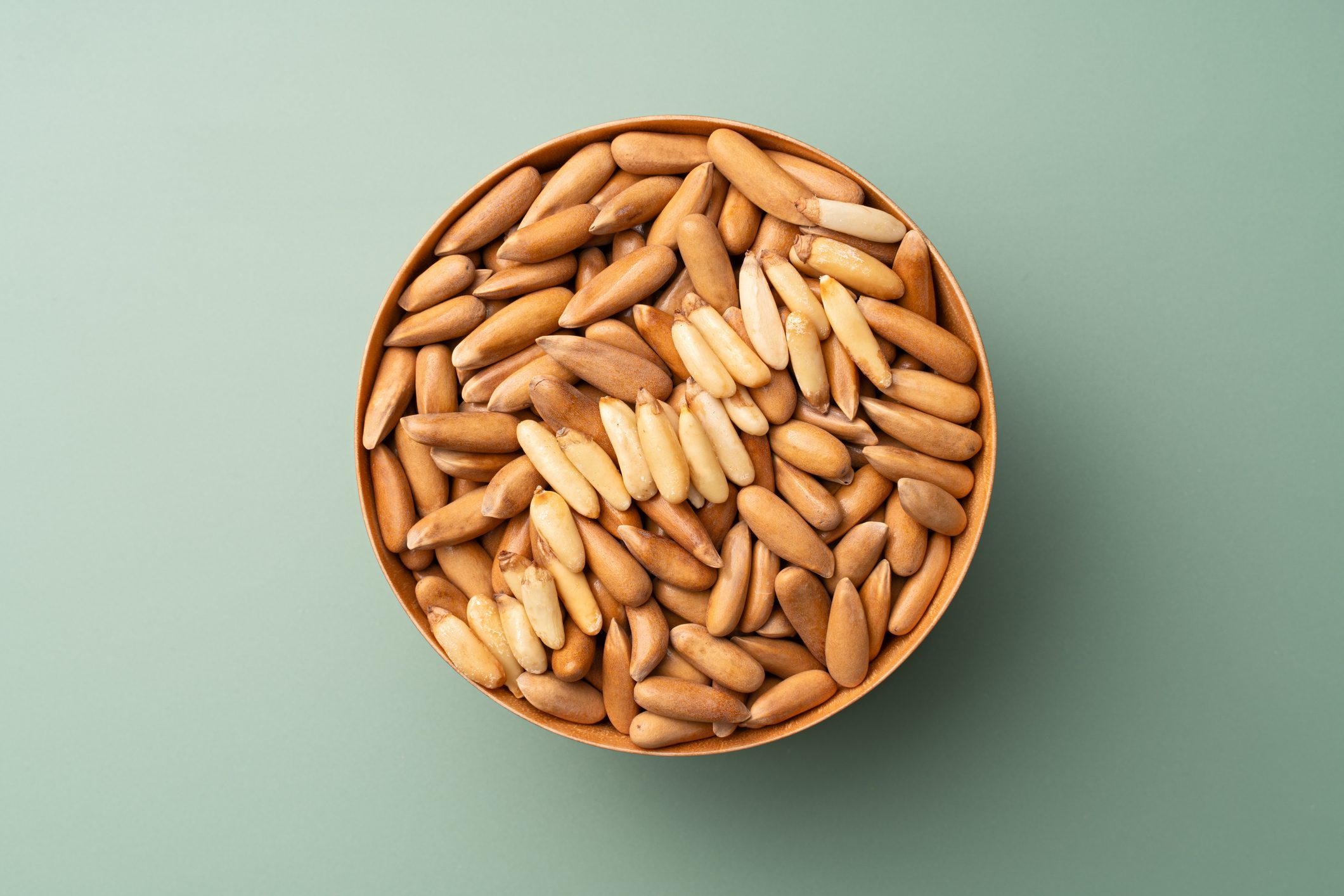 Shelled Chilgoza Pine Nuts in Wooden Bowl on Green Background