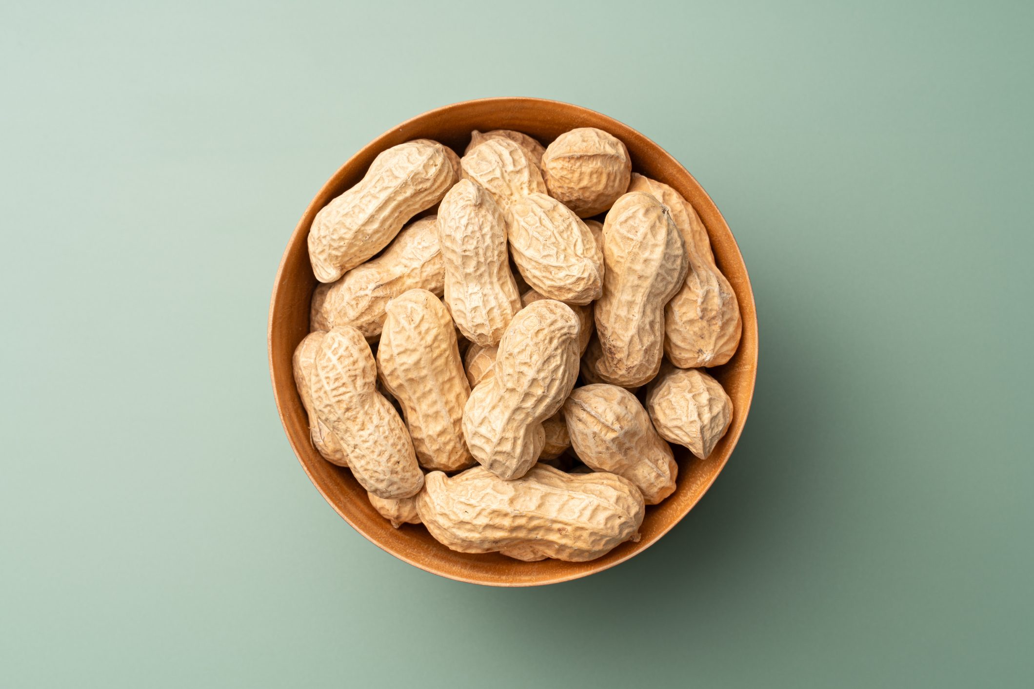 Whole Peanuts in Wooden Bowl on Green Background