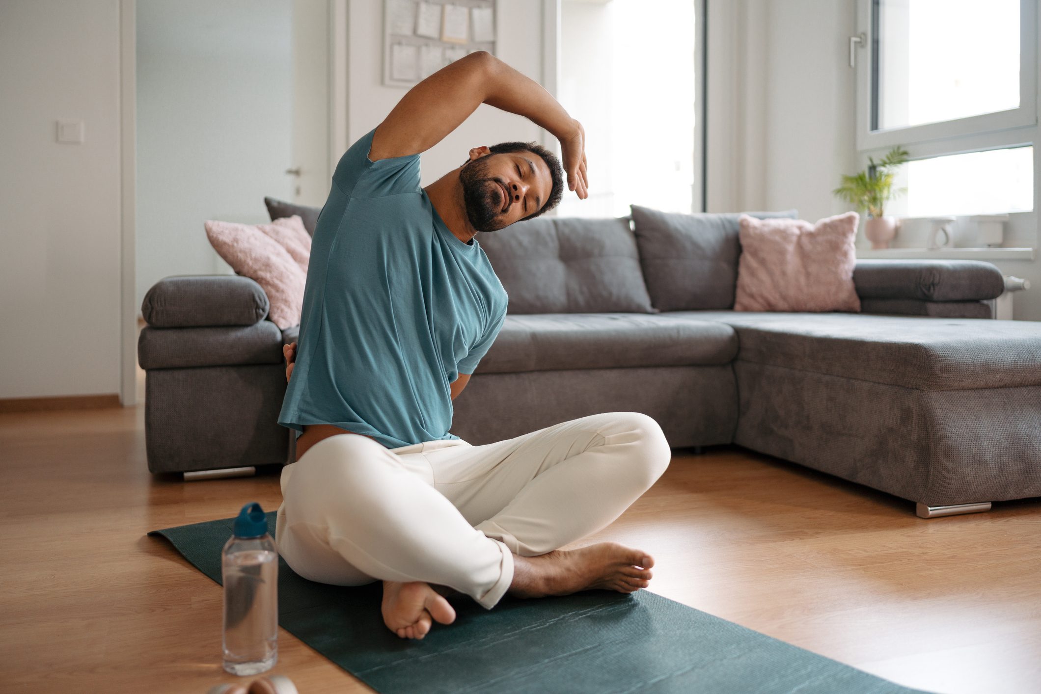 The single man exercising alone at home, stretching his back and arm. Young man is happy, relaxed, and content with his life. Solo home workout and meditation, morning or evening workout routine.
